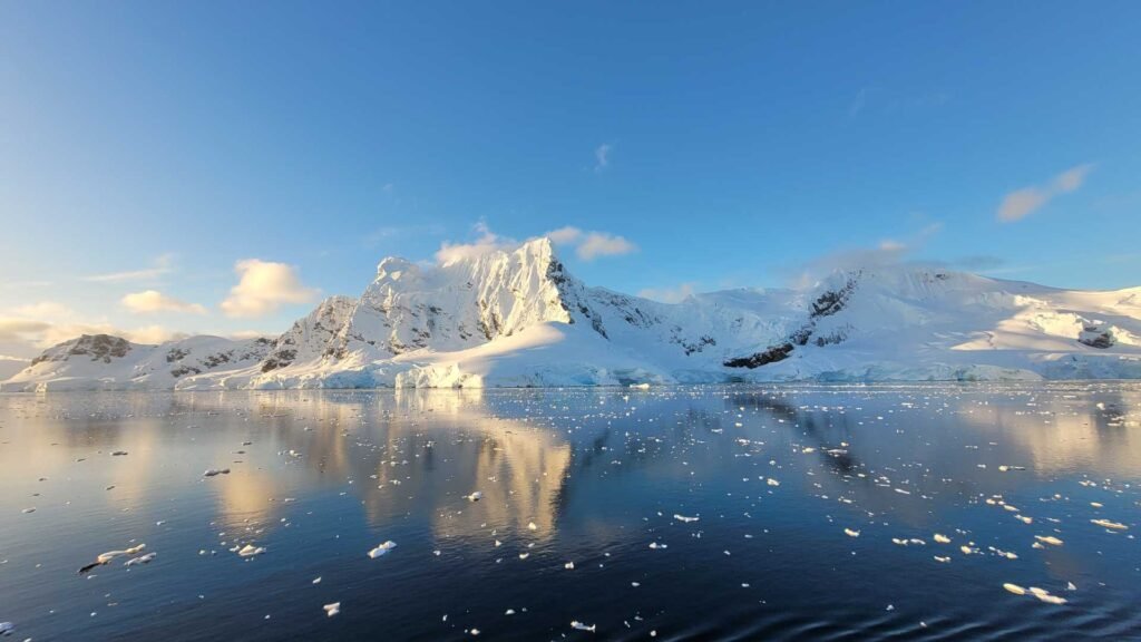 Snowy Antarctic peaks reflect on calm waters, showing the raw beauty of the Peninsula often captured during polar cruises.